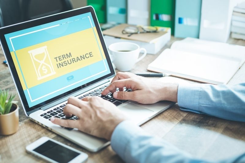 Person using a laptop displaying a term insurance concept on the screen at a desk with coffee and documents.