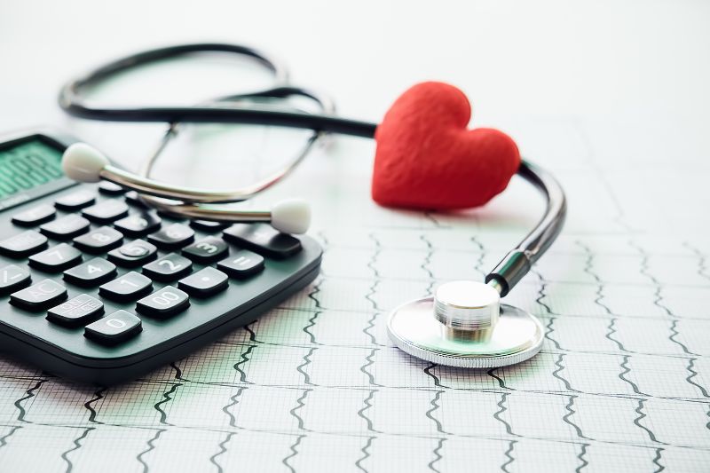 Stethoscope with red heart, calculator, and ECG paper symbolizing health insurance, medical costs, and financial planning